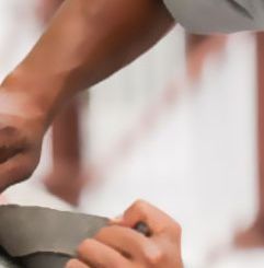 Una persona utiliza una pequeña herramienta de metal para tallar o dar forma cuidadosamente a un trozo de material circular de color gris.