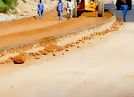 Obreros de la construcción supervisan un proyecto de nivelación de carreteras con maquinaria pesada en un camino cubierto de tierra junto al asfalto pavimentado.