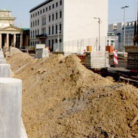 Obra en construcción cerca de la Puerta de Brandeburgo en Berlín, con montones de tierra y materiales de construcción.