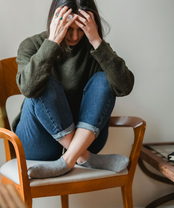 Una persona sentada acurrucada en una silla, con las manos en la cabeza, vestida con un suéter verde