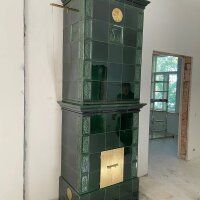 Green tiled stove in a bare room, with a gold door and an open doorway in the background