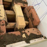 Broken brick wall with fallen bricks, dirt, and debris beside a white panel wall