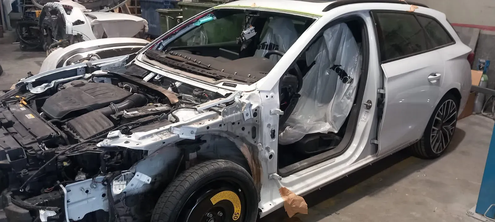 Un coche blanco está siendo desmantelado en un garaje.