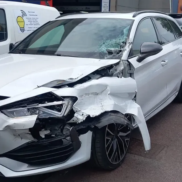 Un coche blanco con la parte delantera dañada está aparcado al costado de la carretera.