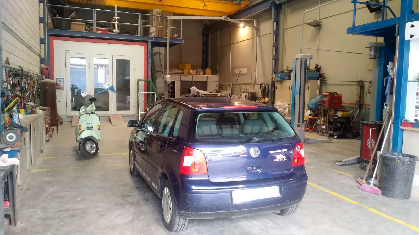 Un coche azul está aparcado en un garaje al lado de un scooter verde.