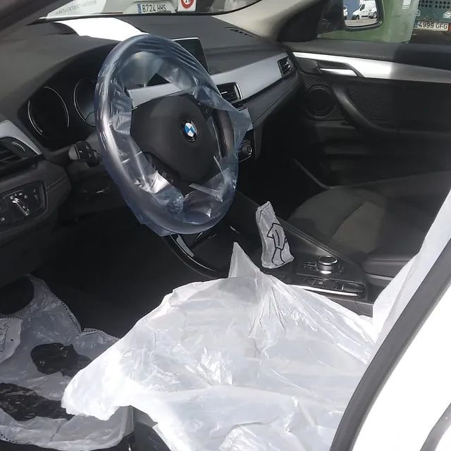El interior de un BMW blanco con el volante envuelto en plástico.