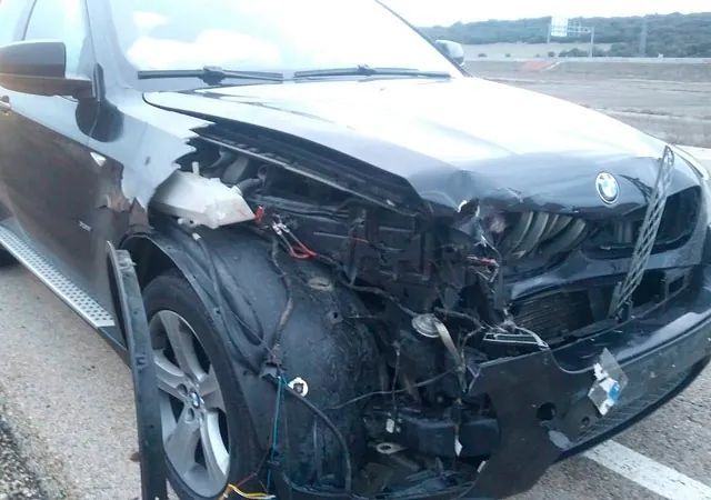 Un coche negro con la parte delantera dañada está aparcado en un estacionamiento.
