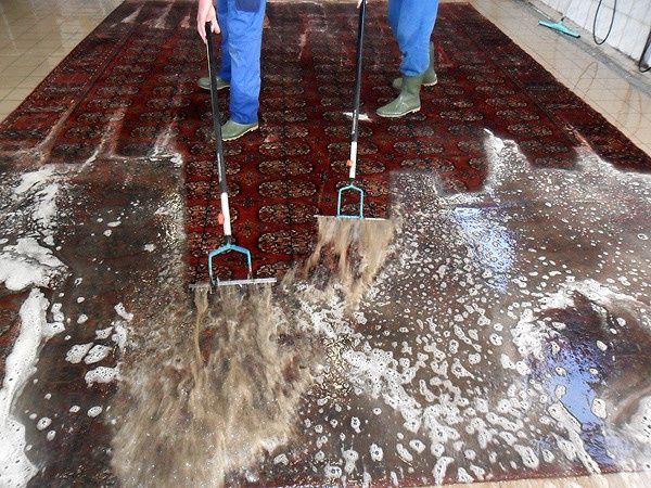 Zwei Personen reinigen einen Teppich mit Wischmopp und Besen.