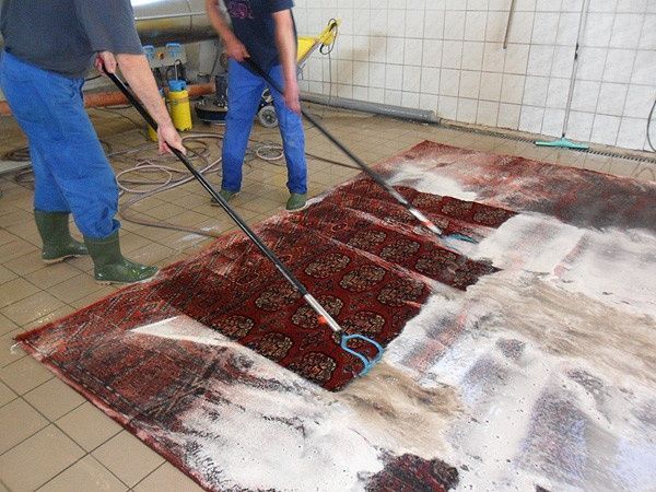 Zwei Männer reinigen einen Teppich mit einem Mopp