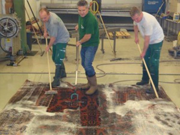 Eine Gruppe von Männern reinigt einen Teppich in einem Zimmer