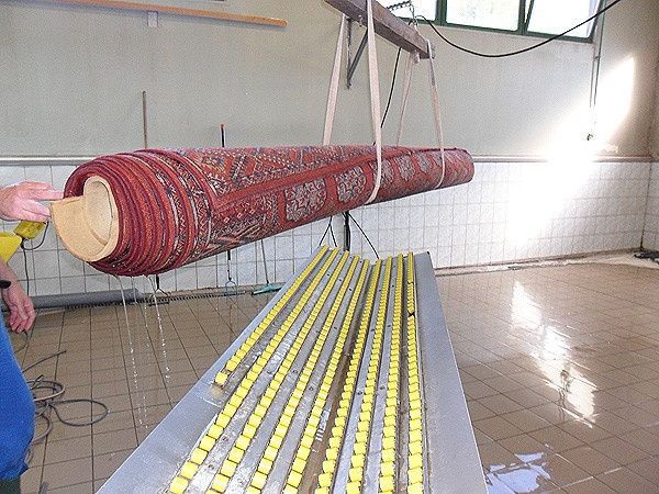 Ein roter Teppich hängt an einem Kran über einem Tisch mit gelben Perlen.