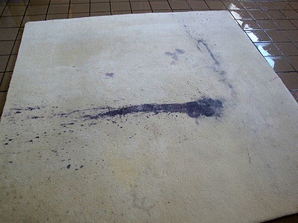 Auf einem gefliesten Boden liegt ein weißer Teppich mit einem blauen Fleck.