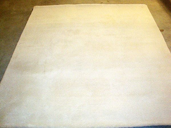 Auf einem Betonboden liegt ein weißer Teppich.