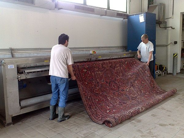 Zwei Männer reinigen in einem Raum mit einer Maschine einen Teppich.