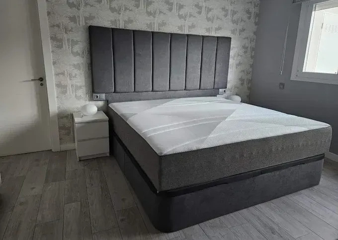 Una cama tapizada en gris con un cabecero alto capitoné vertical