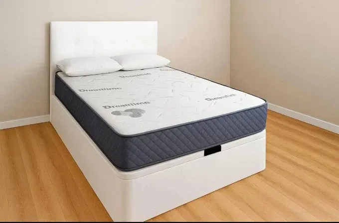 Una cama tapizada en blanco con un colchón gris oscuro