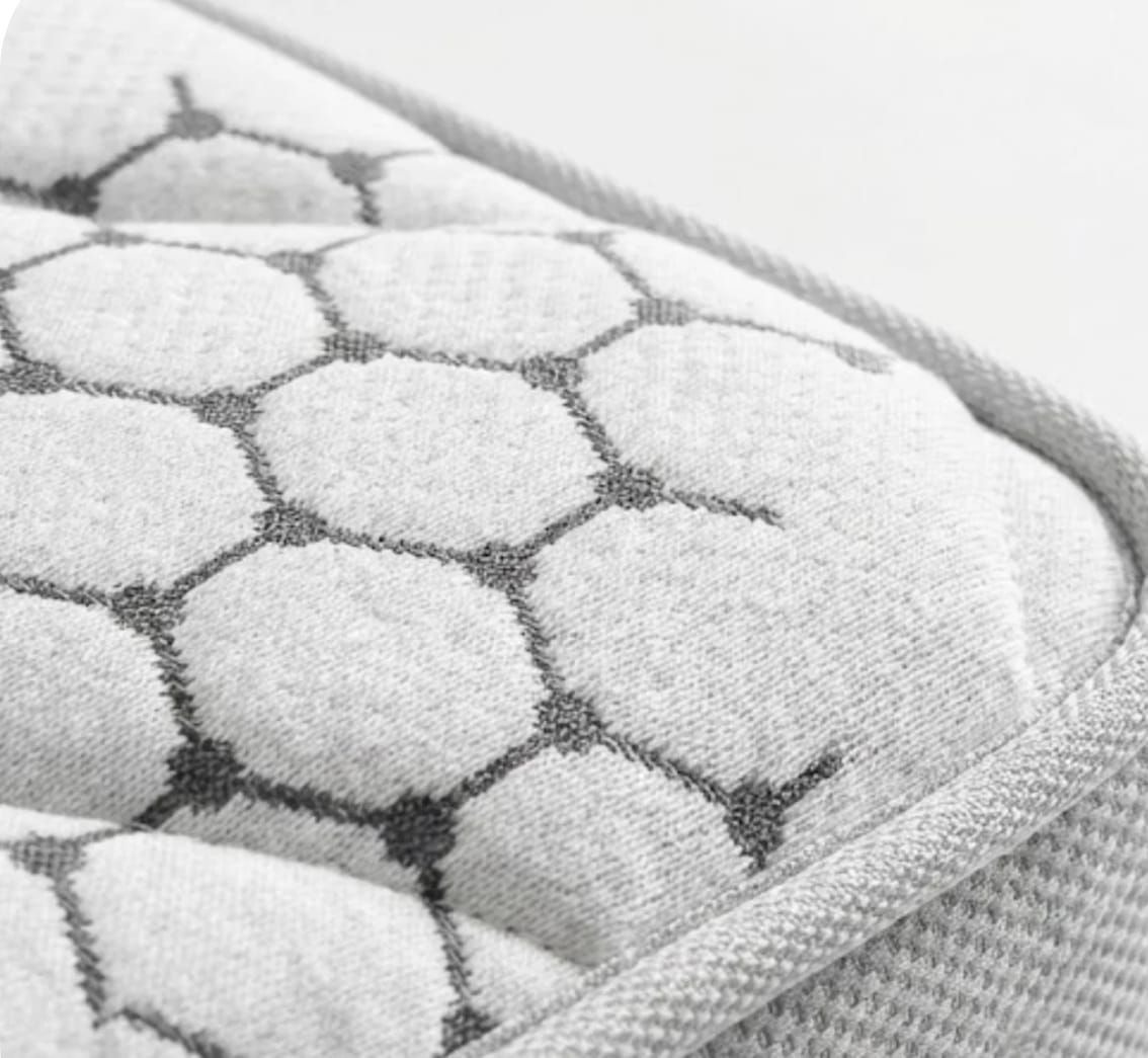 Primer plano de la superficie de un colchón de tela blanca con un estampado hexagonal gris repetitivo y un borde cosido.