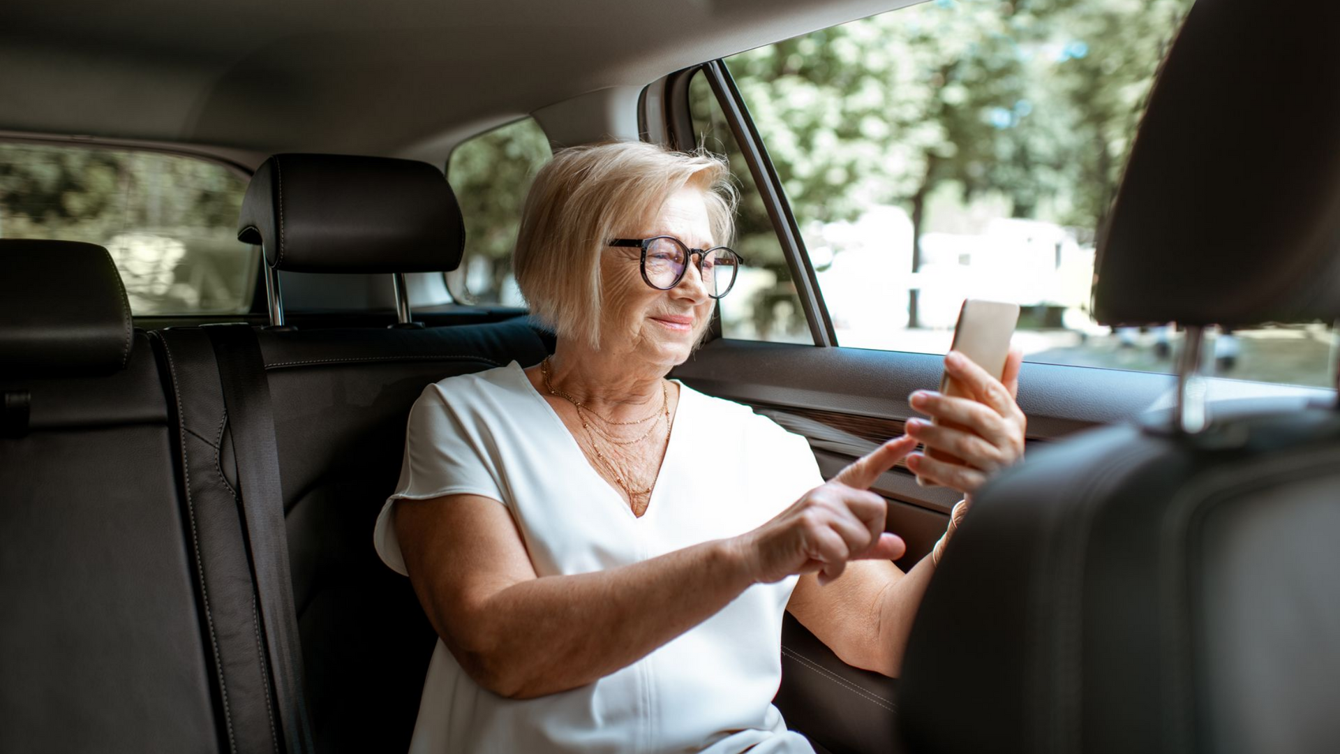 Une personne assise à l'arrière d'une voiture, souriante tout en regardant et en interagissant avec l'écran d'un smartphone.