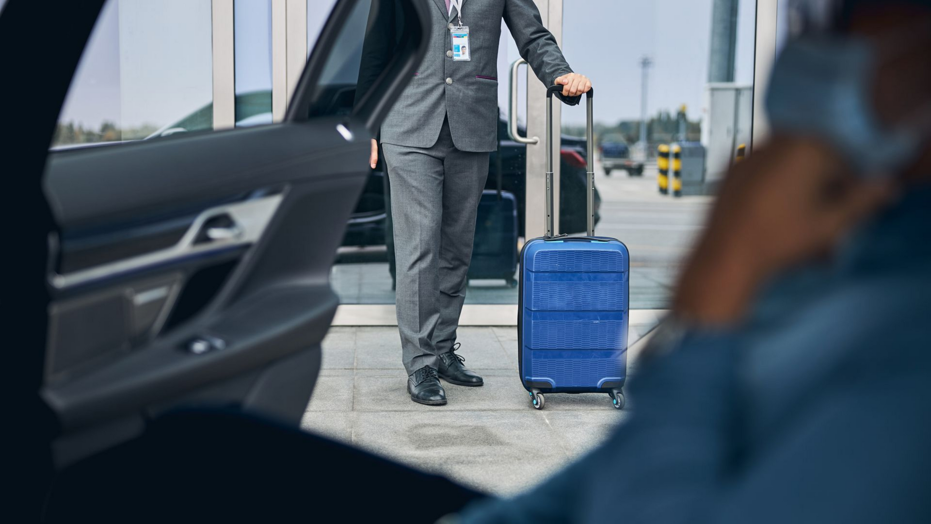 Une personne en costume se tient près d'une portière de voiture ouverte.