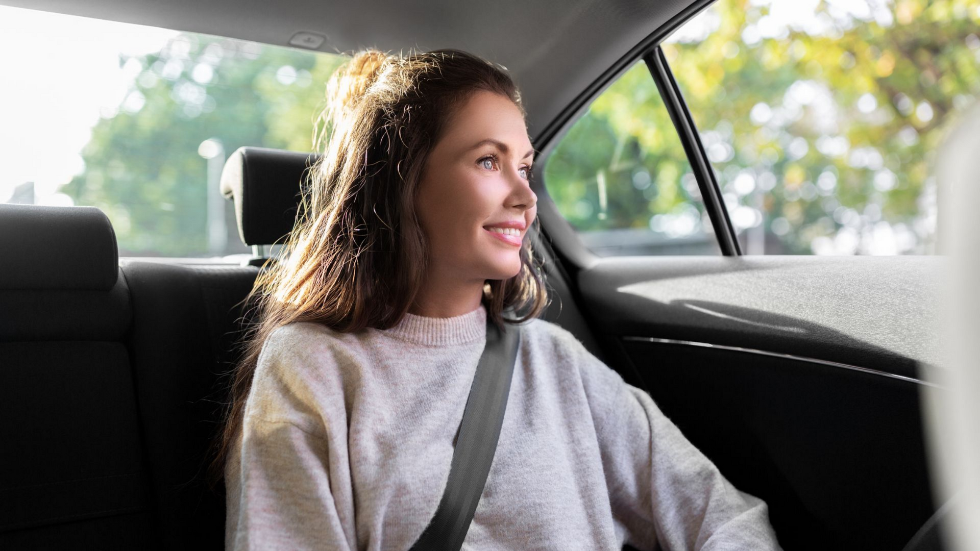 Une personne aux cheveux longs sourit, assise sur la banquette arrière d'une voiture.