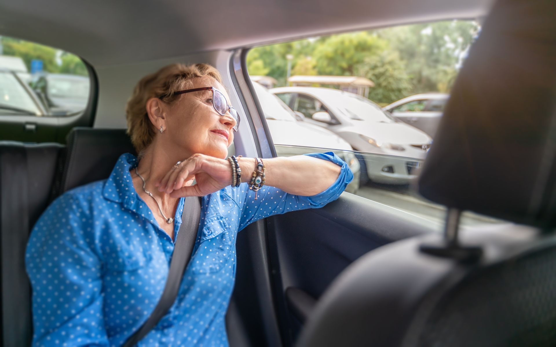 Une personne portant des lunettes et une chemise bleue assise à l'arrière d'une voiture.
