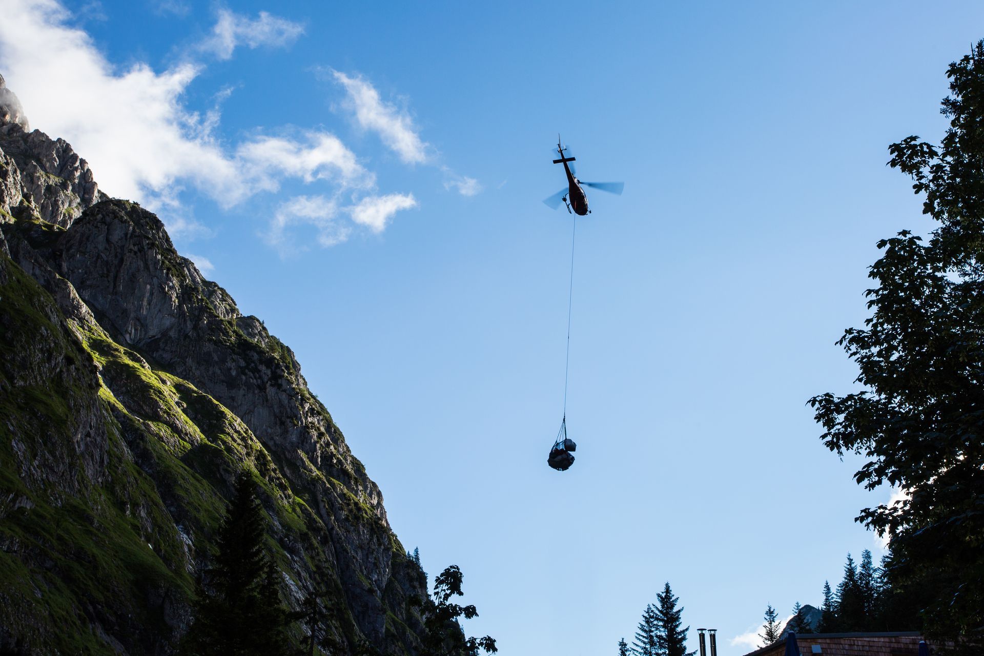 Un hélicoptère dépose une charge suspendue au-dessus d'un canyon rocheux sous un ciel bleu.