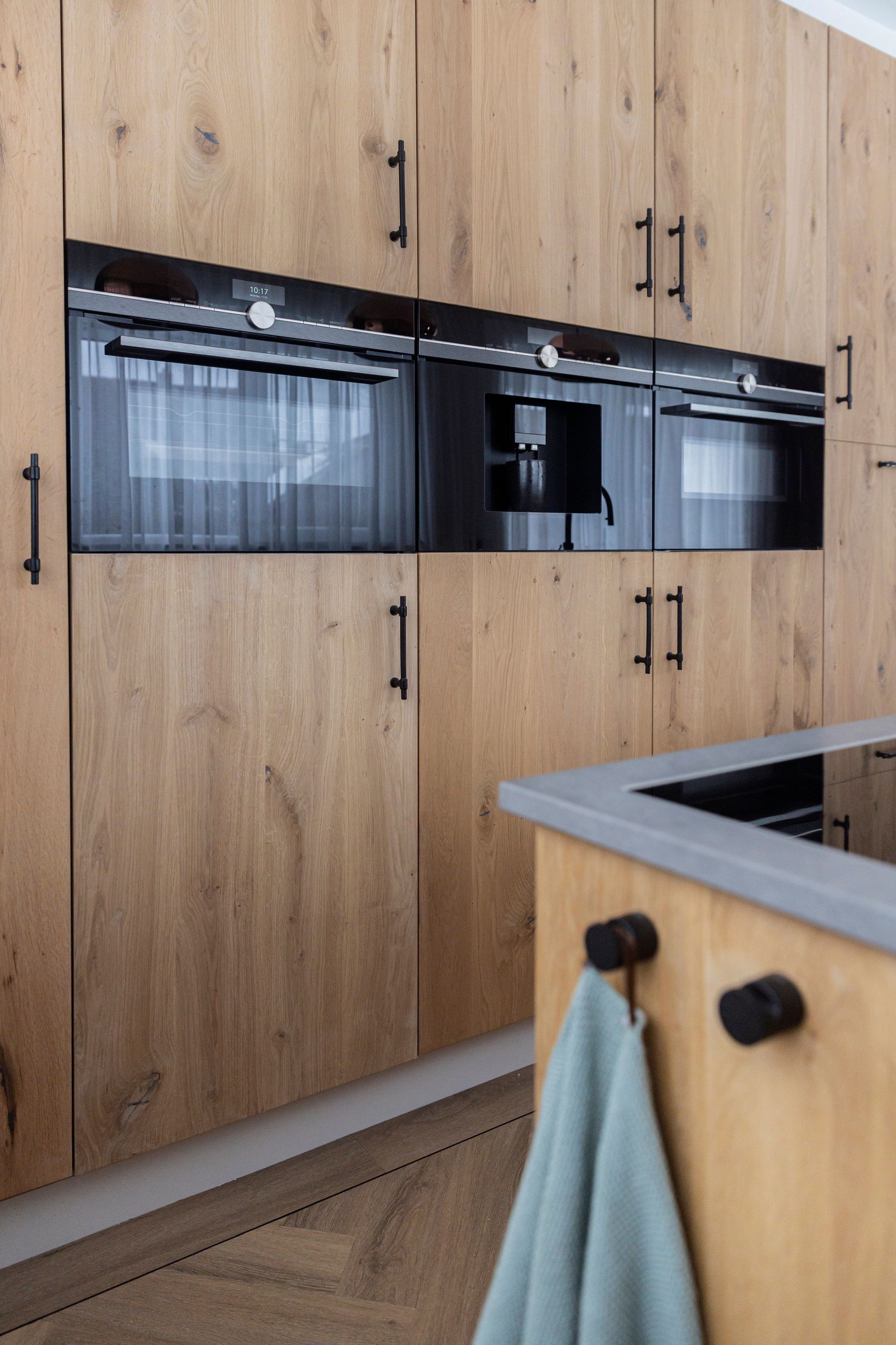 Cuisine moderne avec placards en bois, électroménager encastré noir et îlot central en bois clair avec porte-serviettes.