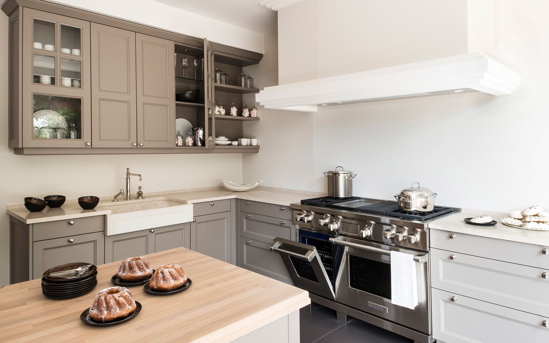 Cuisine moderne et lumineuse avec placards gris, hotte blanche et pâtisseries sur un îlot en bois.