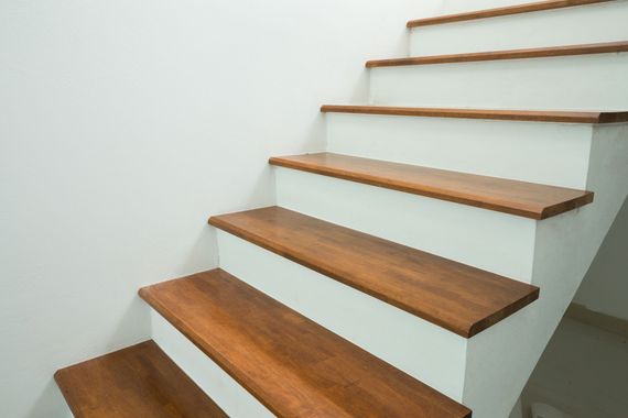 Escalier en bois avec des murs blancs et des marches marron, vu d’en bas.