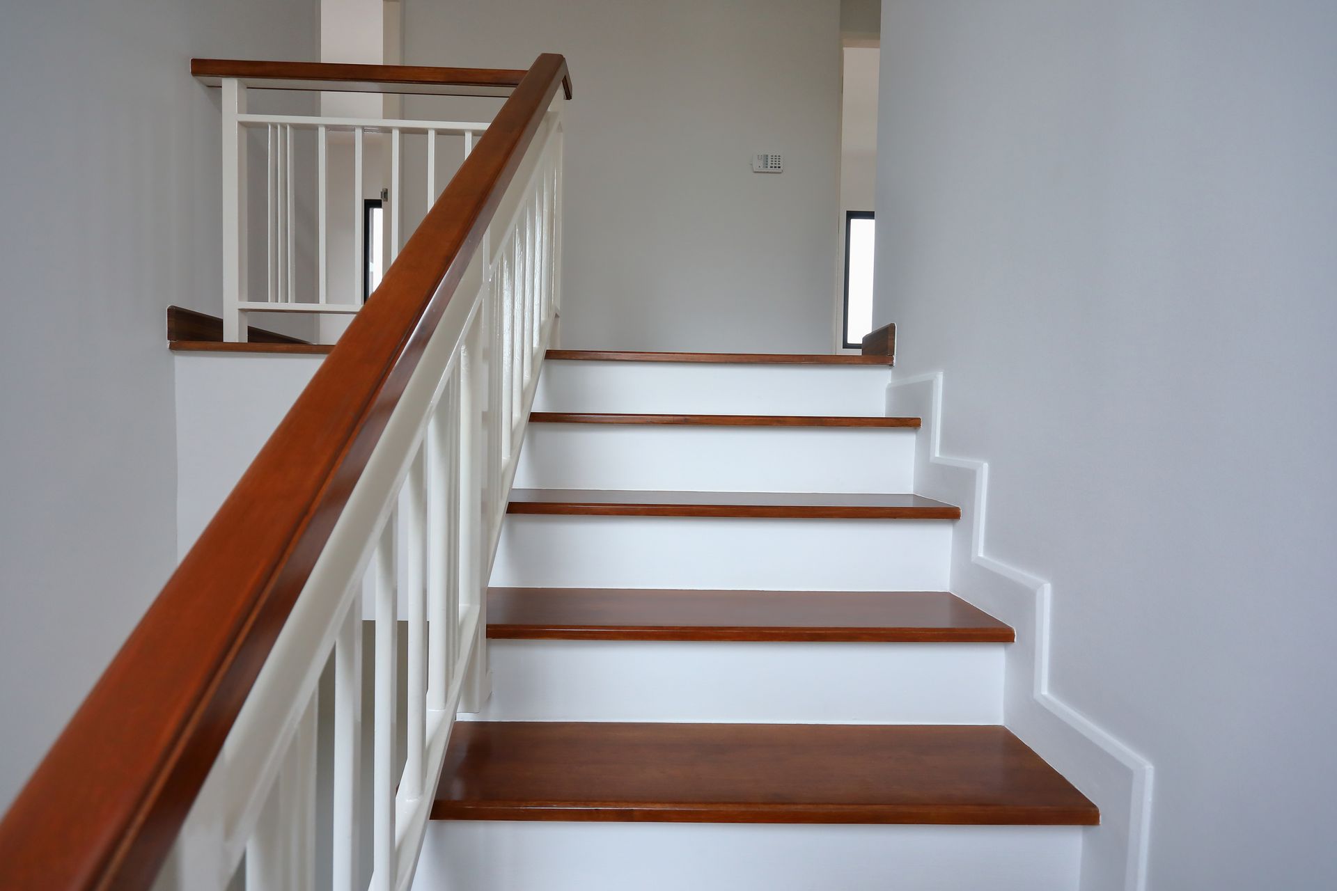 Escalier blanc avec rampe en bois et marches marron dans un couloir intérieur lumineux