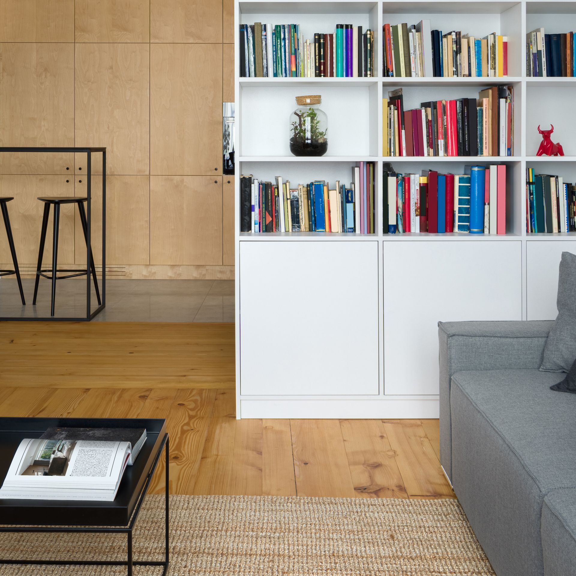 Salon moderne avec canapé gris, bibliothèque blanche, parquet et table basse, à côté d’un coin repas