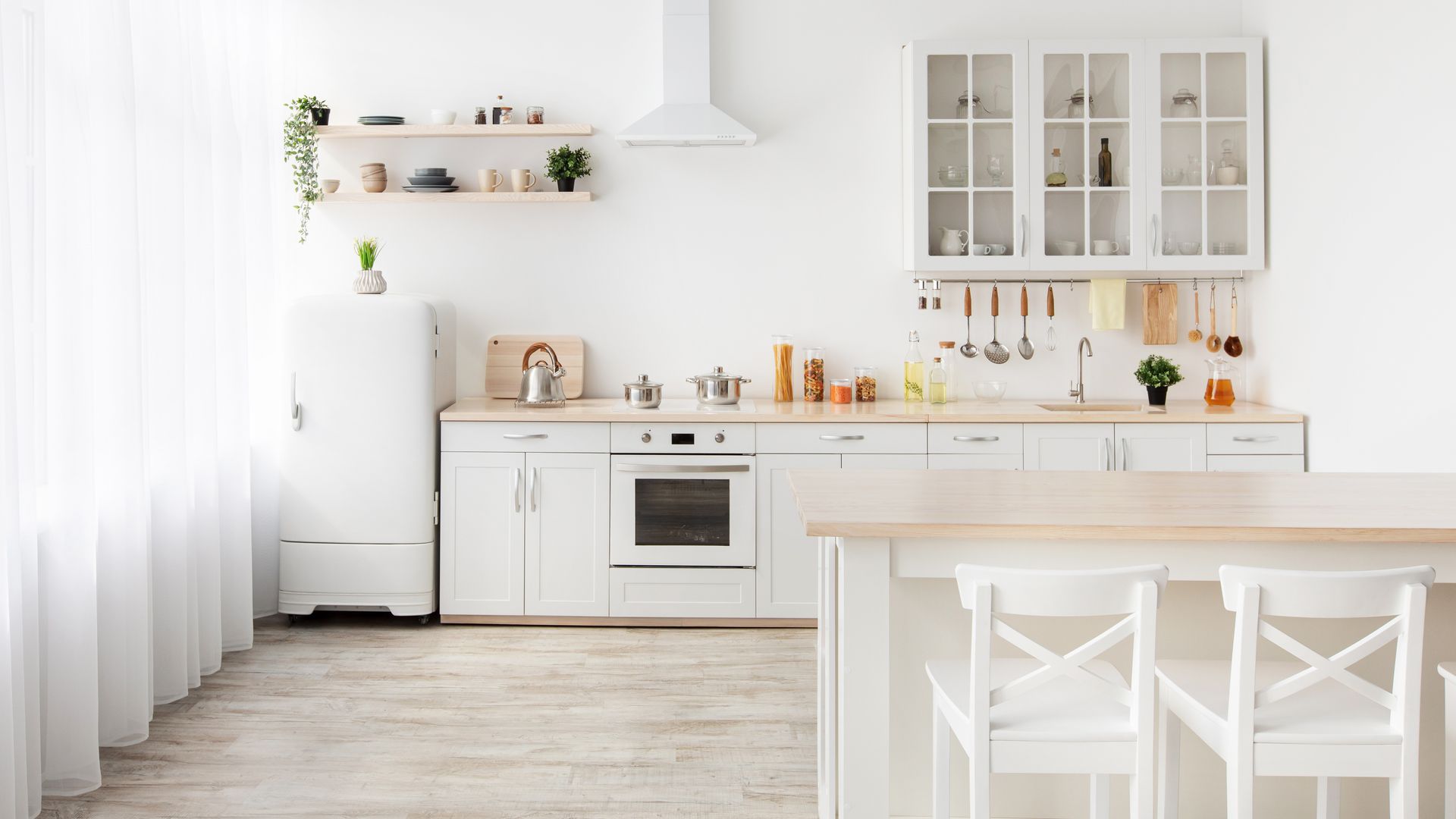 Cuisine moderne d’un blanc éclatant, avec îlot central, placards et étagères ouvertes, dans une pièce baignée de soleil