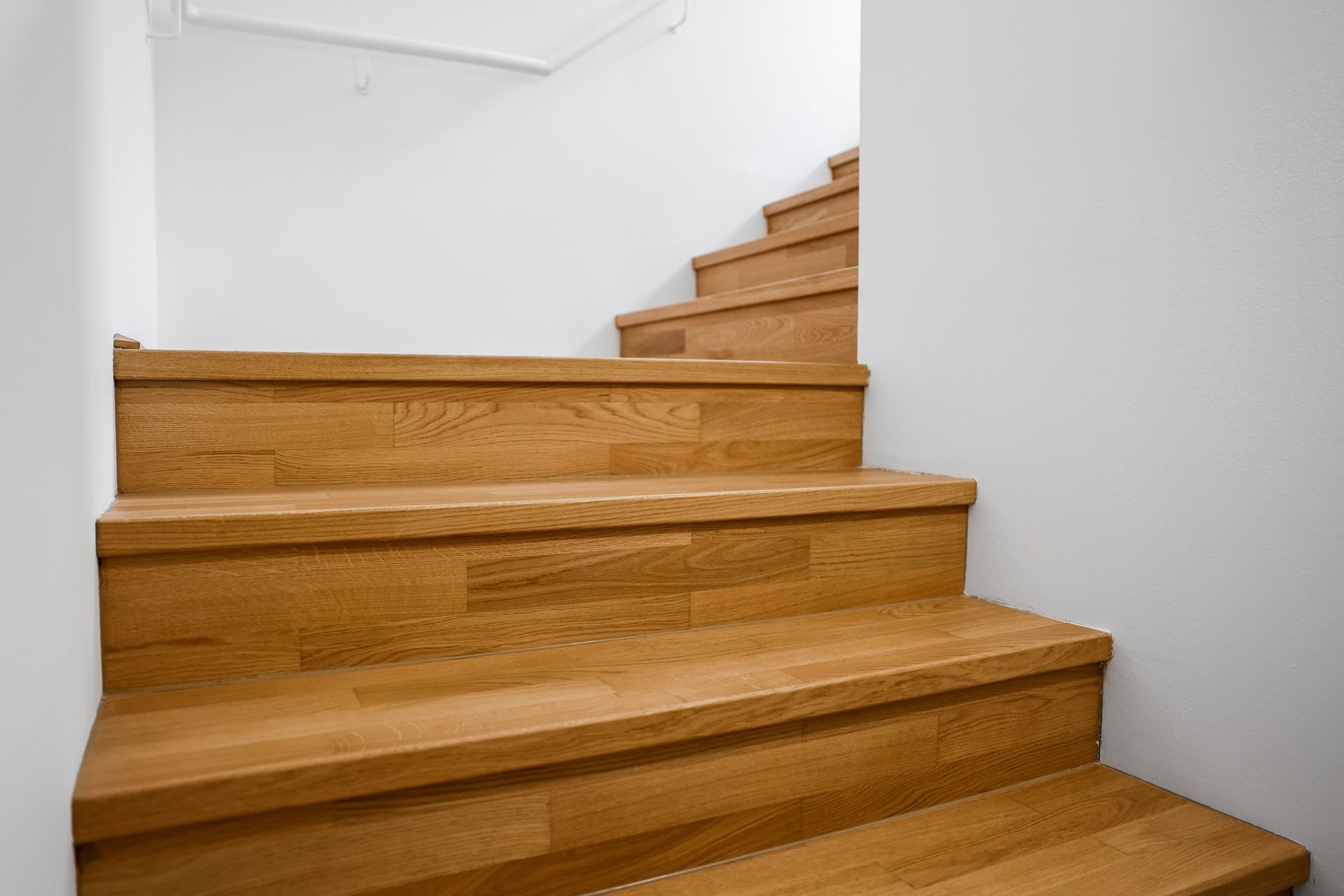 Escalier en bois avec des murs blancs et des marches aux tons chauds dans un intérieur lumineux.