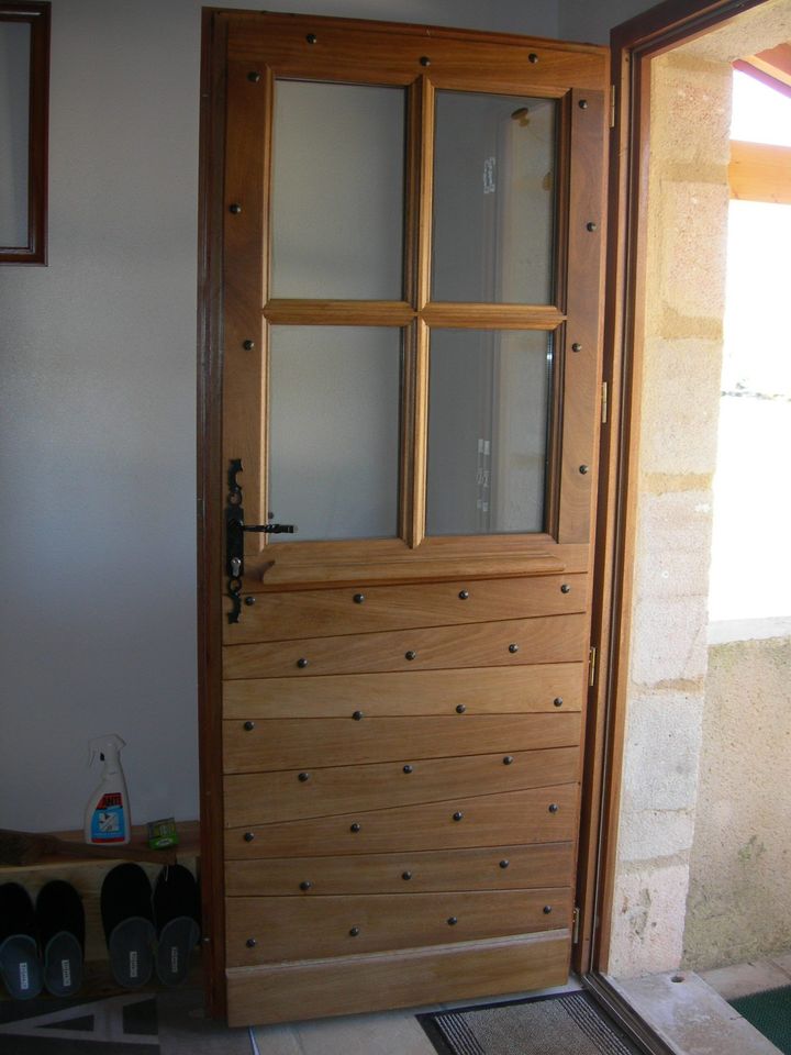 Porte en bois avec des vitres, entrouverte, donnant sur l’extérieur depuis une entrée carrelée