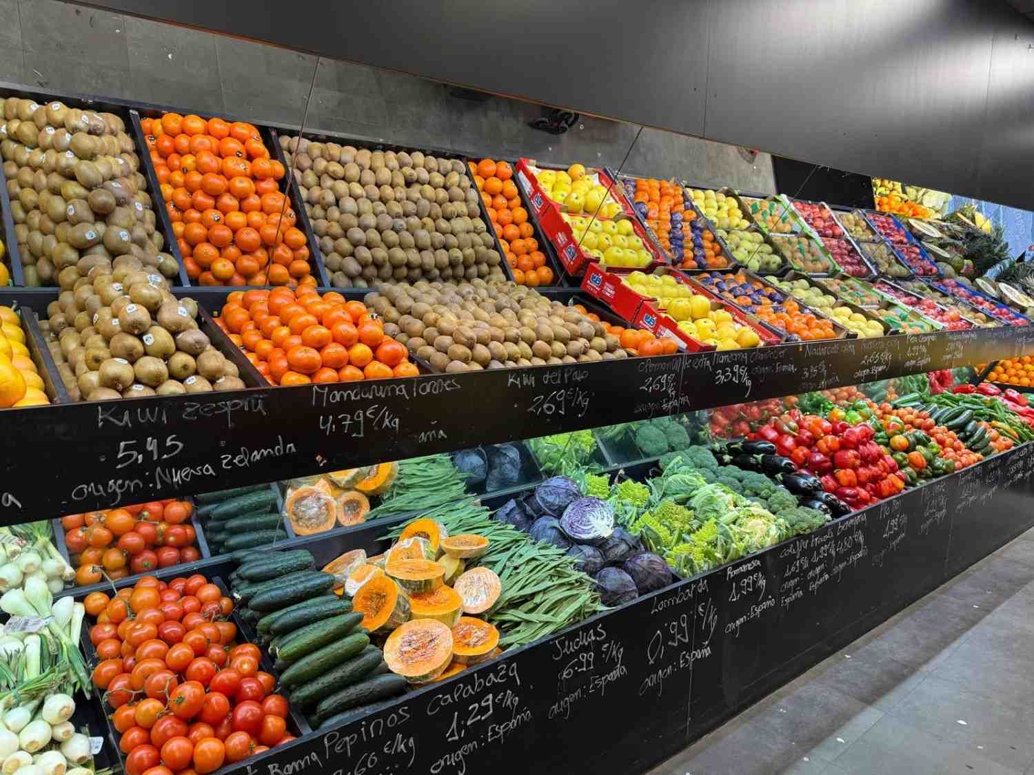 Exhibición de productos en un mercado; naranjas, kiwis, tomates y otras frutas y verduras en cajas de madera.