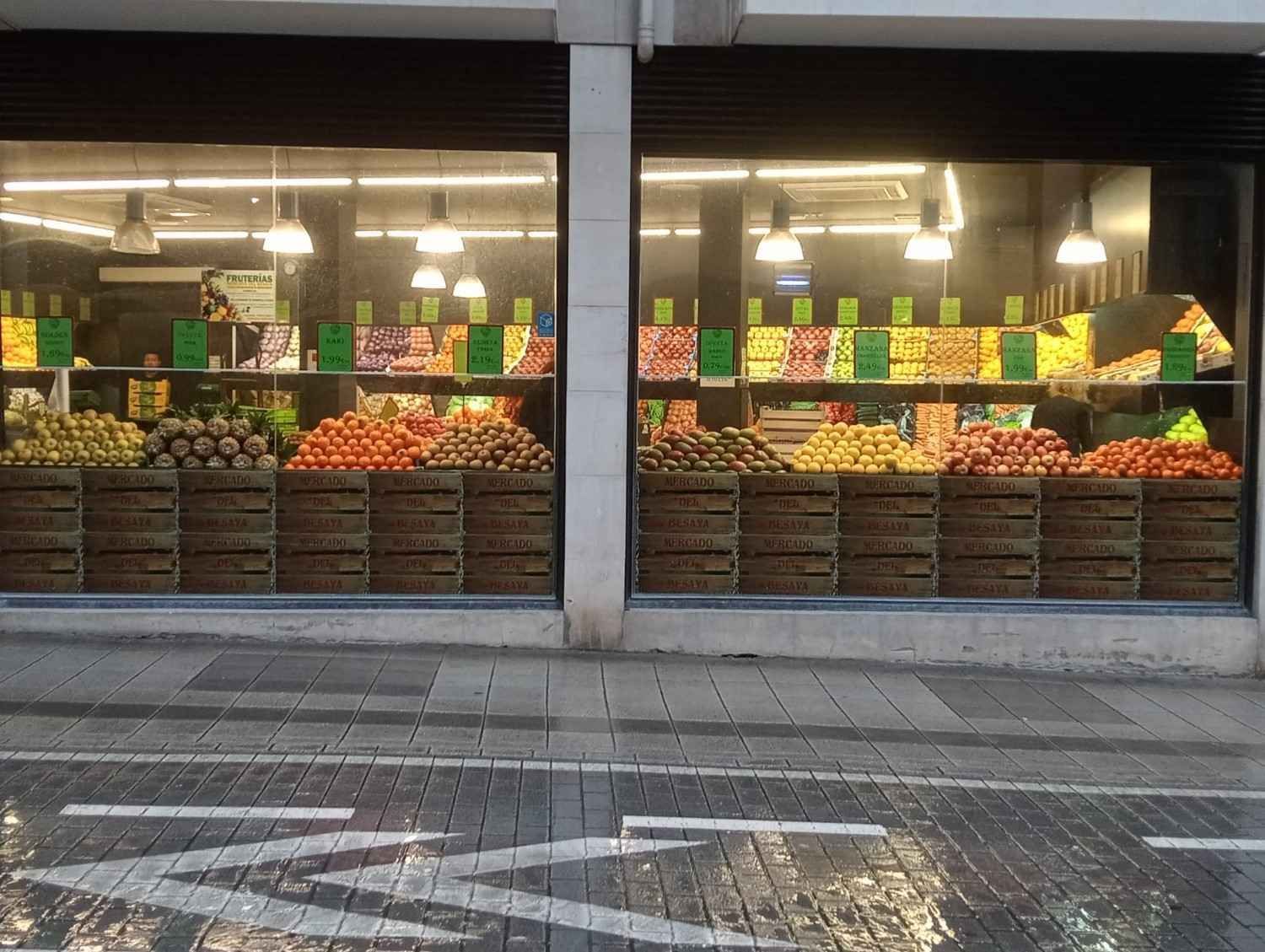 Tienda de productos agrícolas con cajas de productos expuestas detrás de grandes ventanales que reflejan la calle.