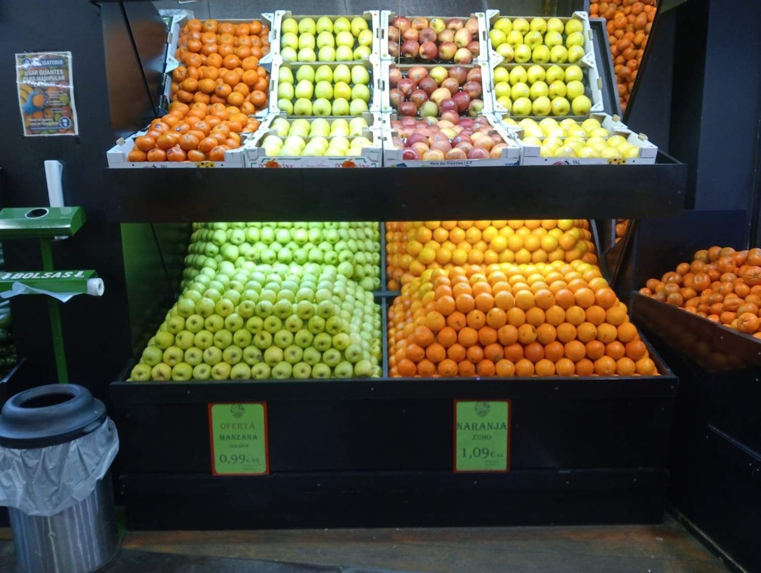 Exhibición de frutas: naranjas, manzanas y manzanas verdes dispuestas en cajas de madera escalonadas en una tienda.