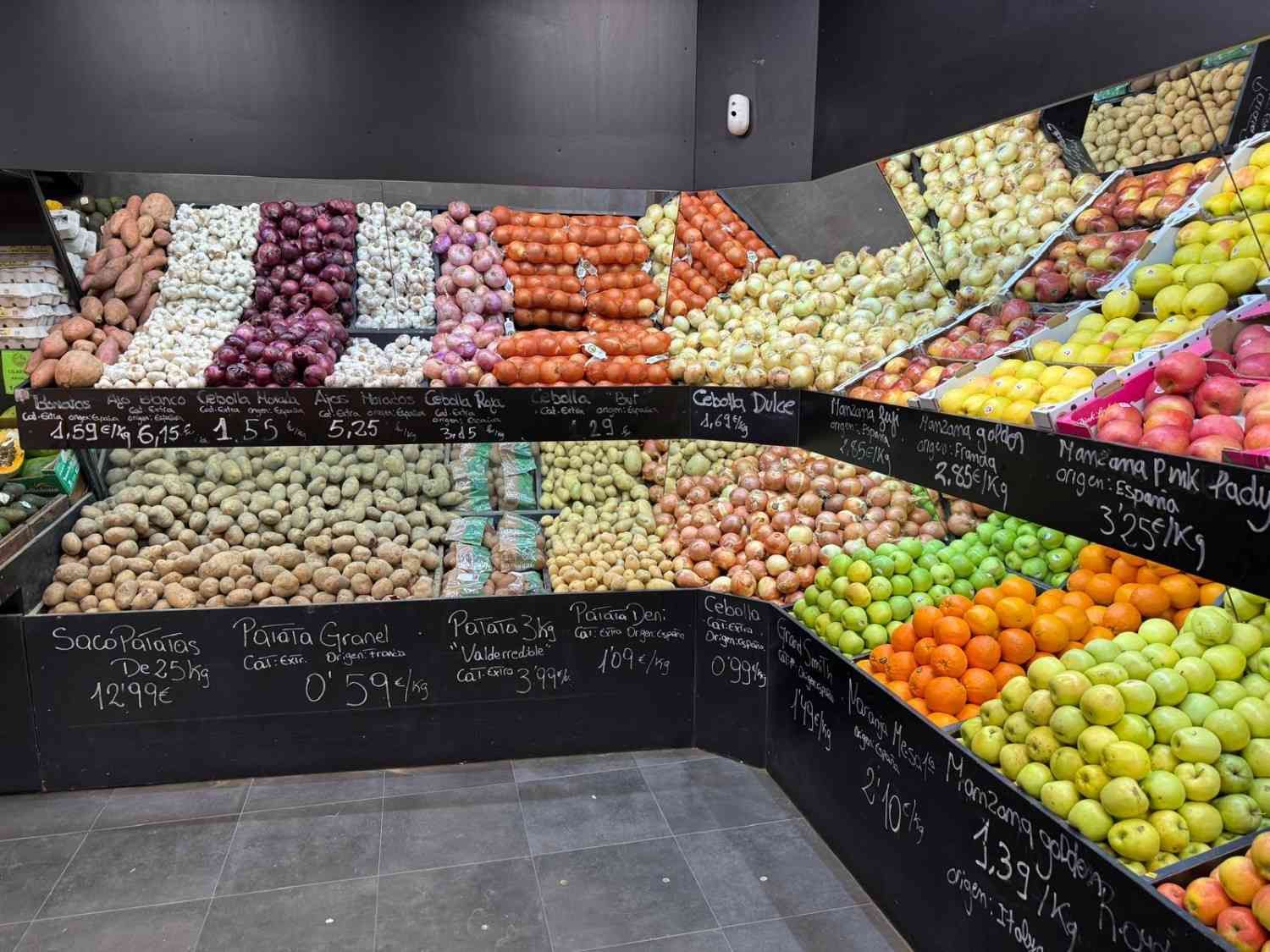 Exposición de productos en una tienda de comestibles, con diversas frutas y verduras en contenedores.