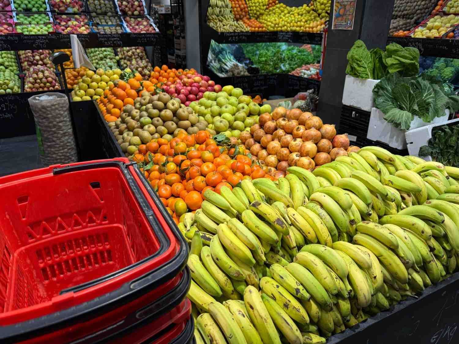 Exhibición de frutas y verduras frescas en un mercado, con una cesta de compra roja en primer plano.