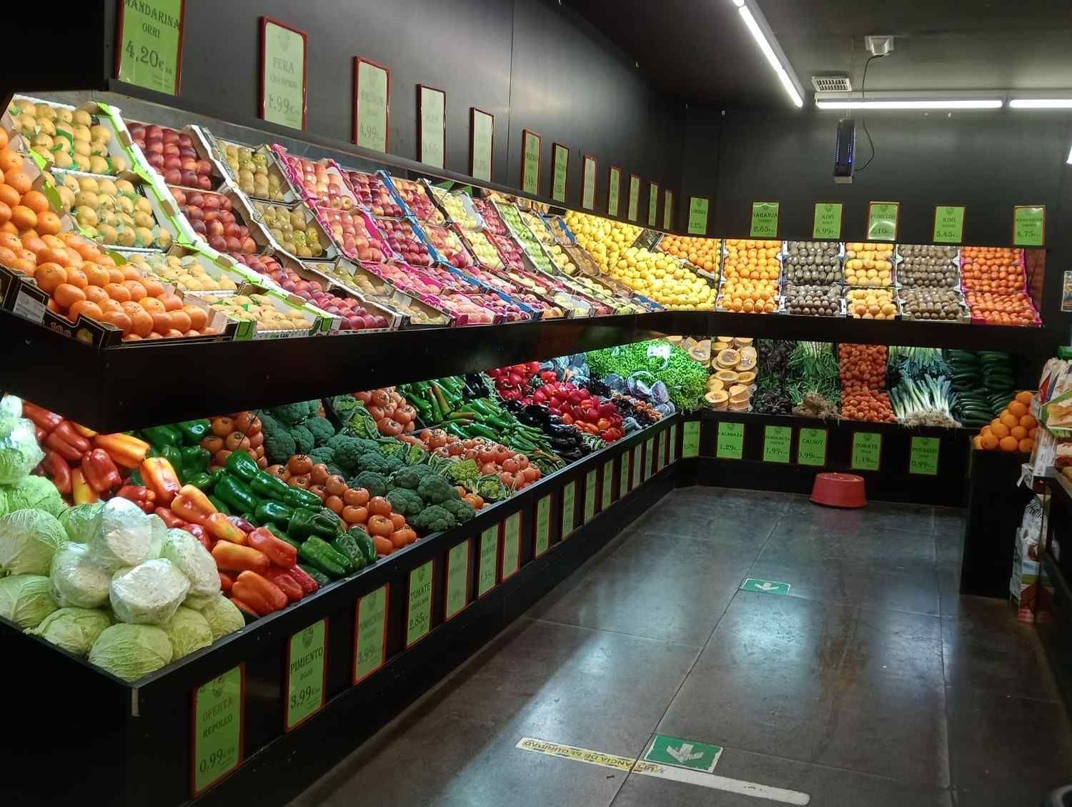Pasillo de productos agrícolas en una tienda de comestibles, repleto de frutas y verduras frescas.