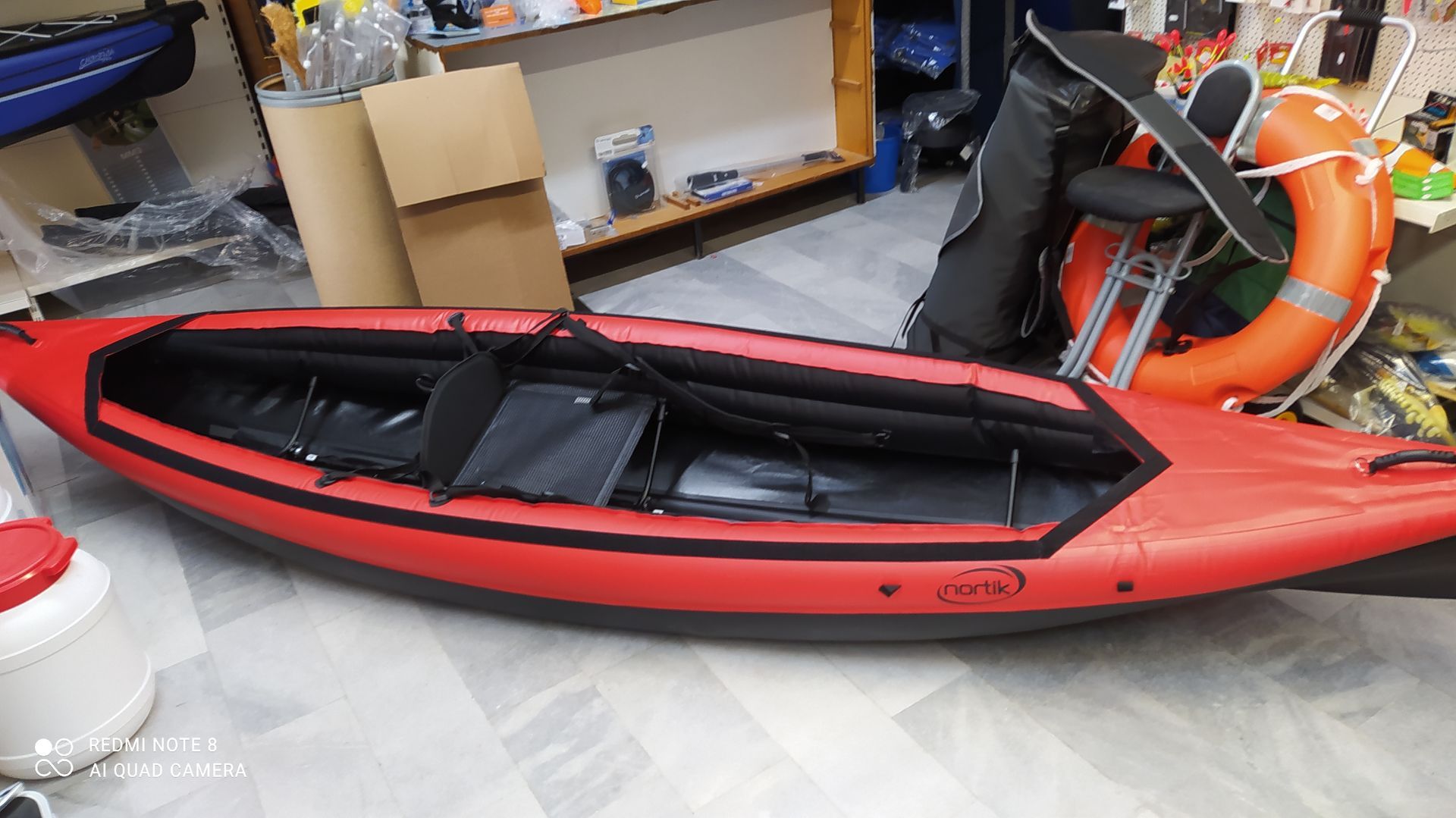 In einem Zimmer steht ein rot-schwarzes Kajak auf dem Boden.