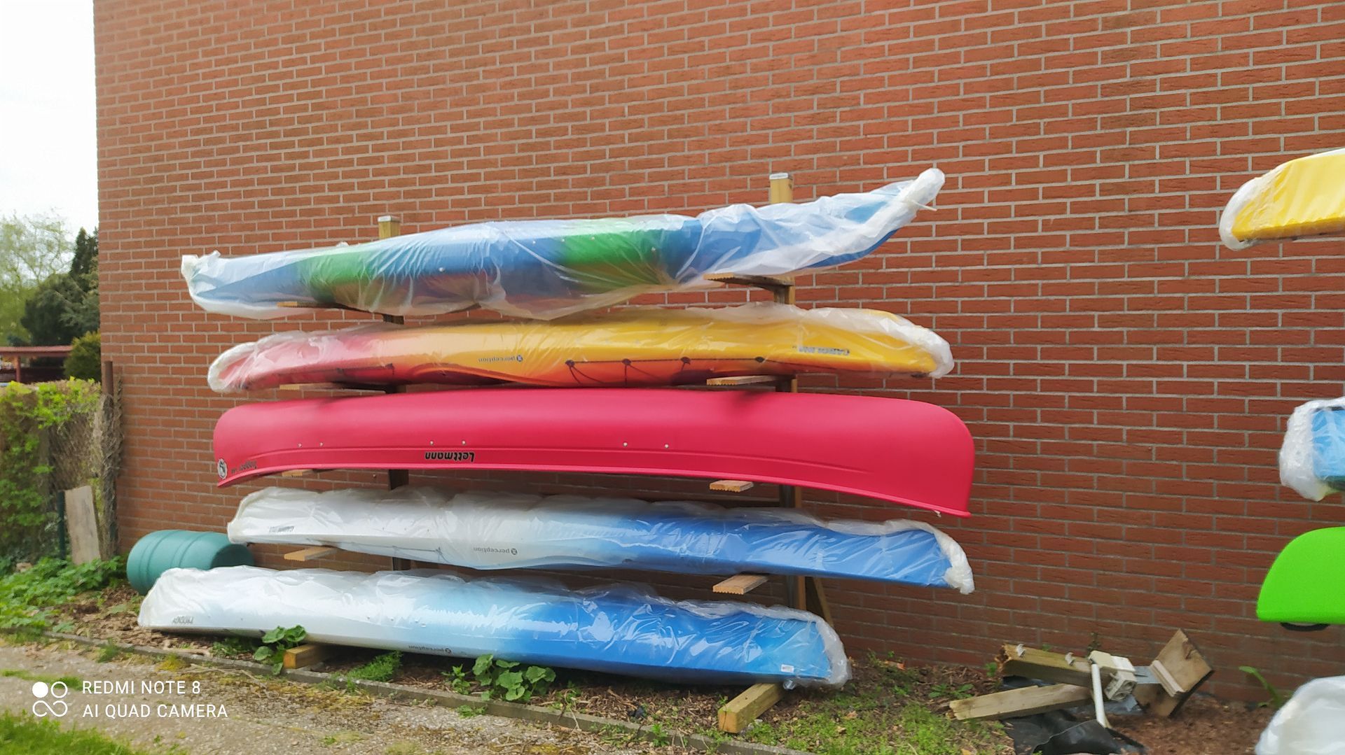 Vor einer Backsteinmauer sind mehrere Kanus übereinander gestapelt.