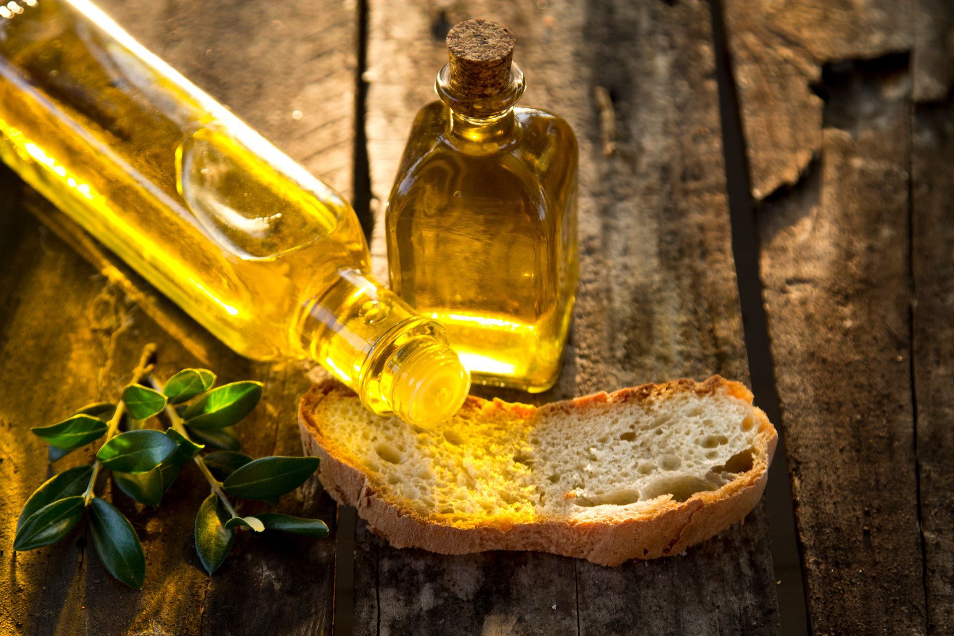 Bouteilles d'huile d'olive, tranche de pain et feuilles d'olivier sur une table rustique en bois