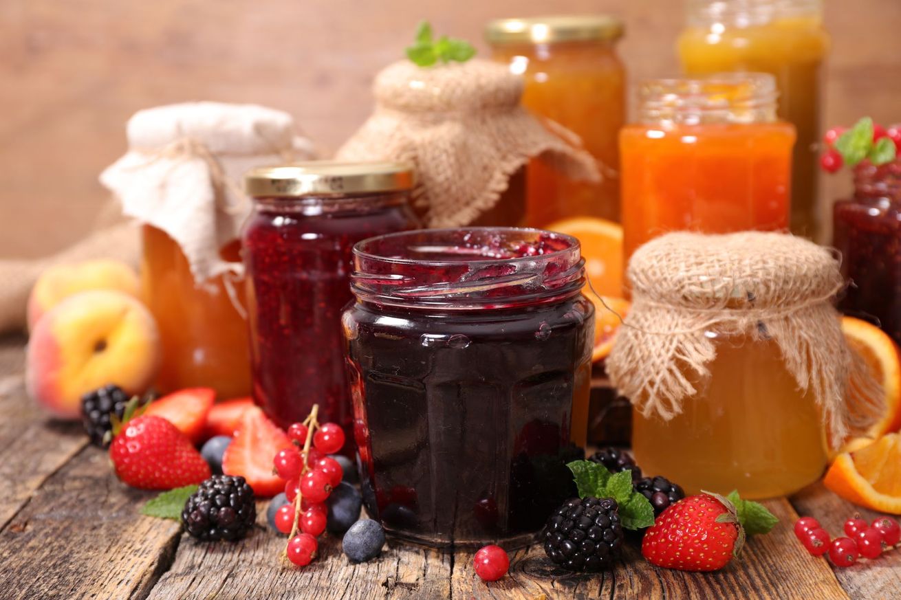 Des pots de confitures et de conserves de fruits maison (fraises, mûres et pêches) sur une table en bois