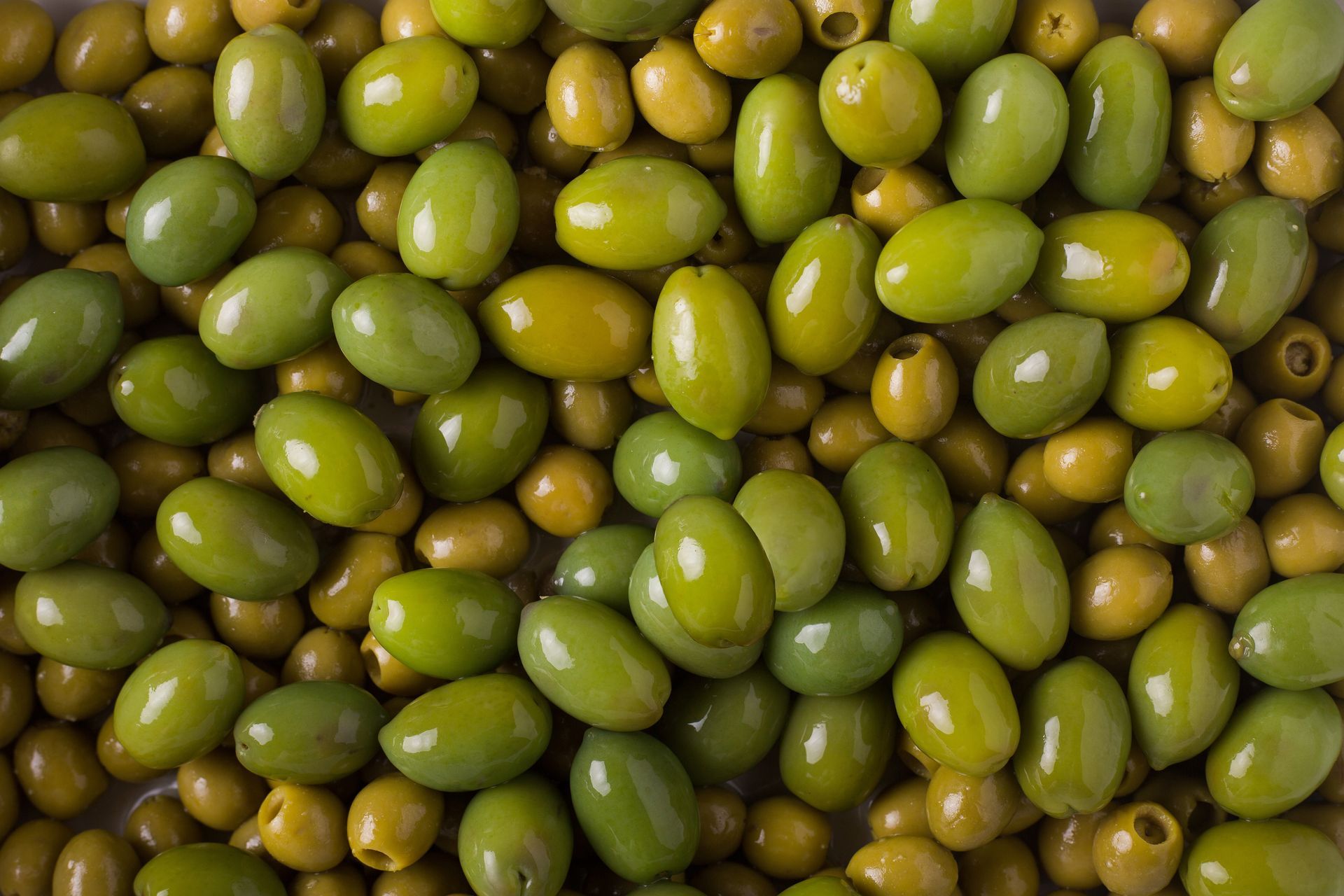 Gros plan sur des olives vertes empilées, certaines jaunissant et brunissant.