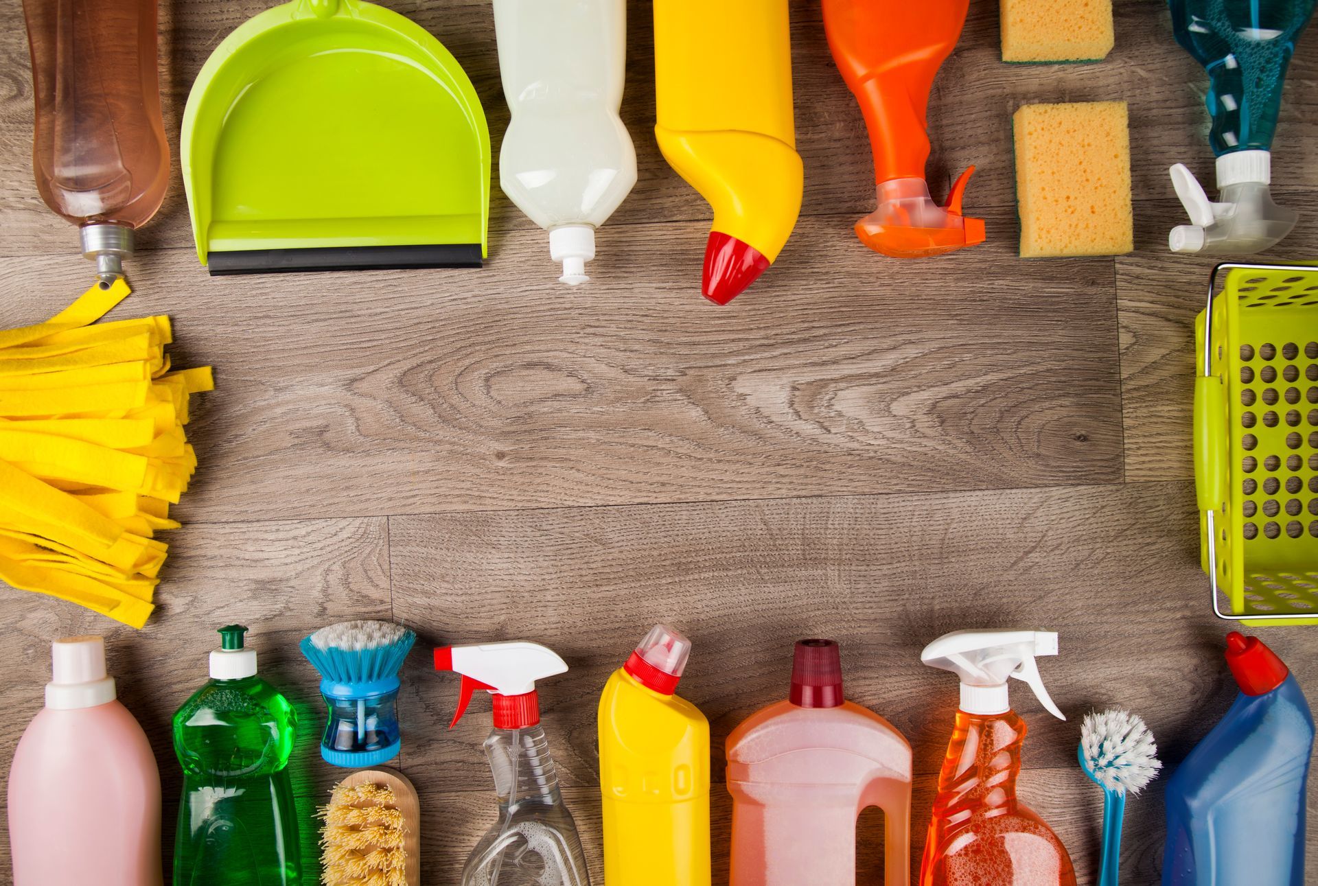 Divers produits de nettoyage colorés disposés à plat autour d'une surface en bois.