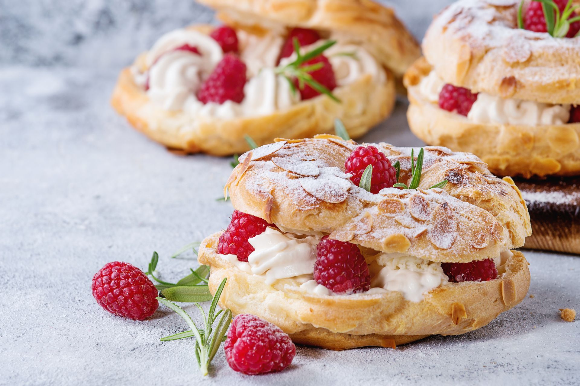 Pâtisseries à la crème en poudre garnies de framboises sur une surface en pierre claire