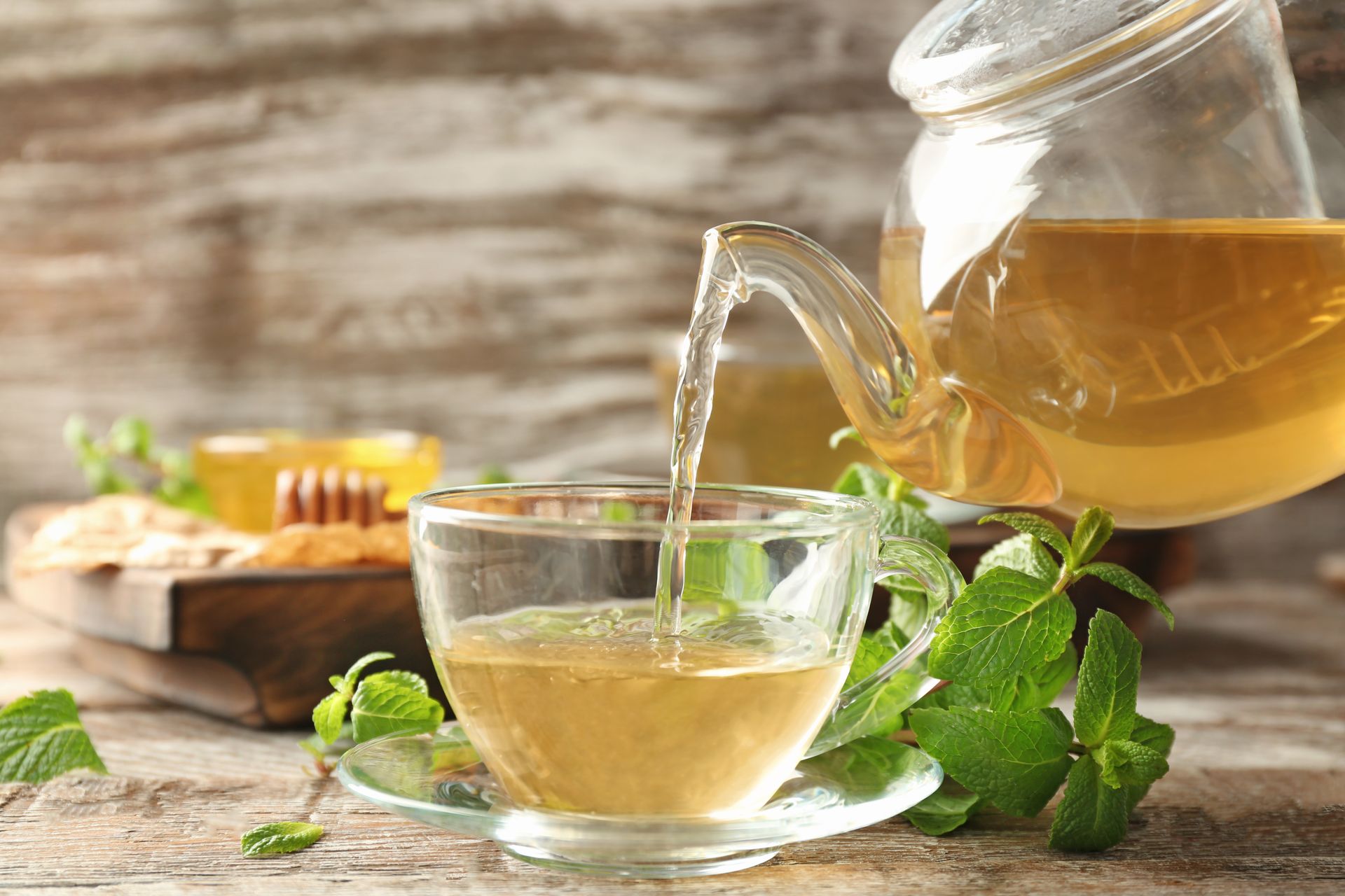 Du thé clair est versé d'une théière en verre dans une tasse avec de la menthe fraîche sur une table en bois.