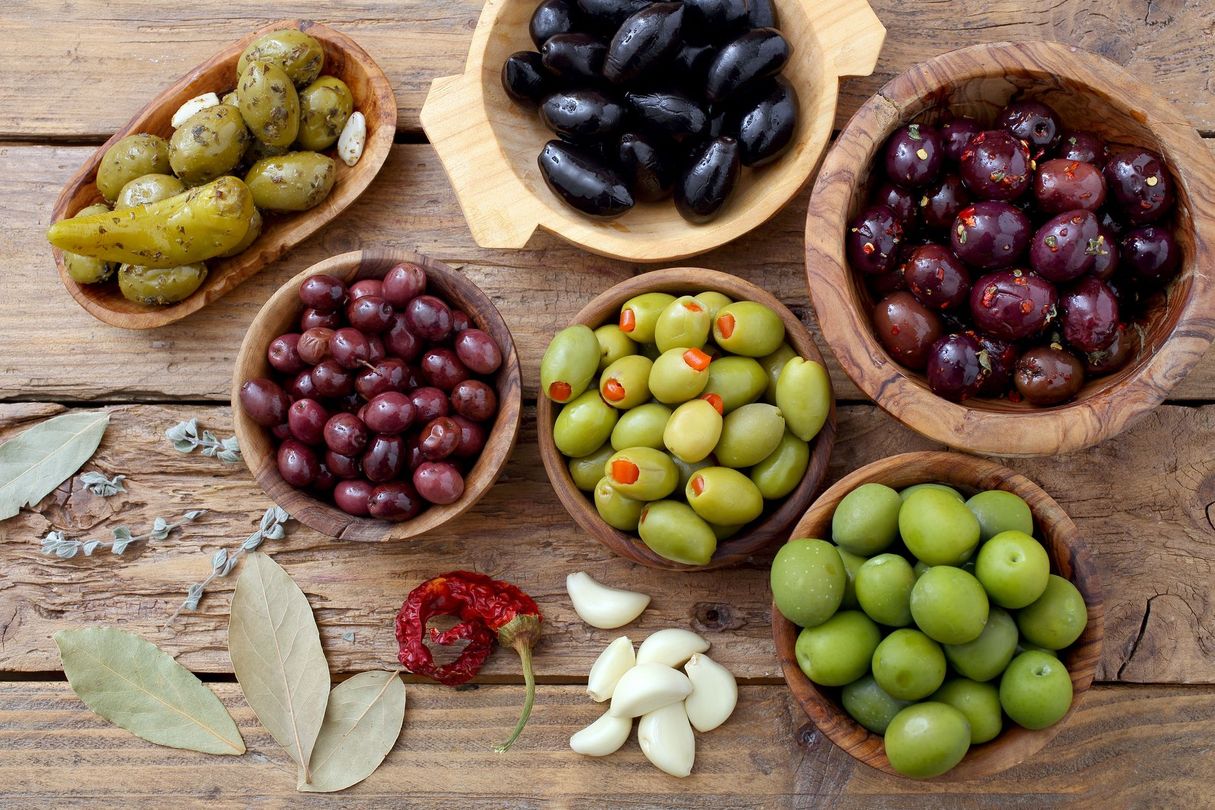 Olives assorties dans des bols en bois avec des feuilles de laurier et de l'ail sur une table rustique