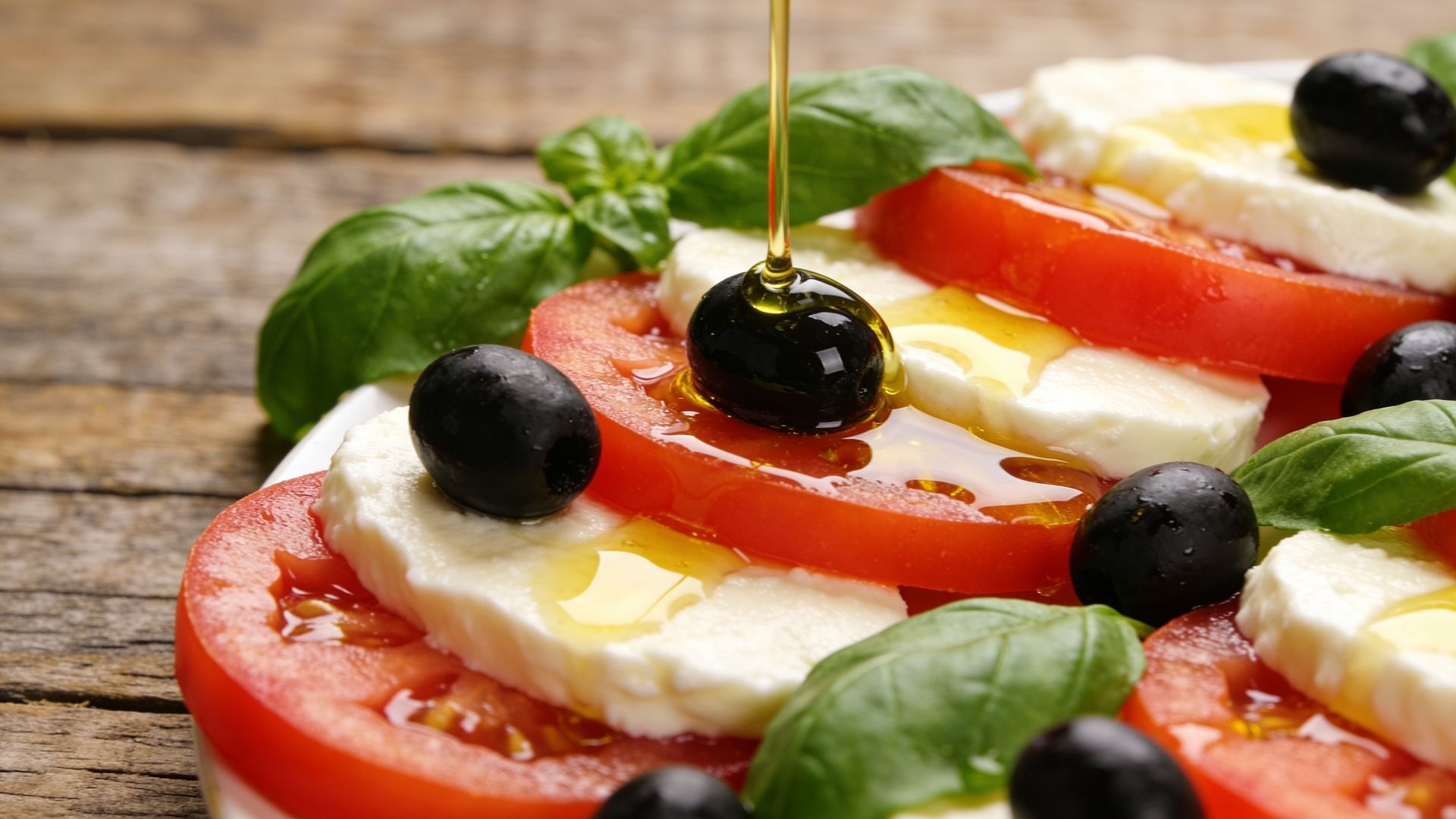 Salade Caprese avec tranches de tomates, mozzarella, basilic, olives et filet d'huile d'olive